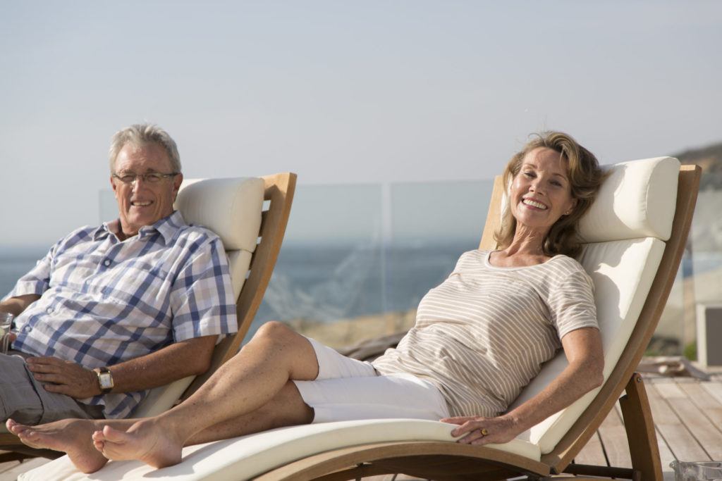 Portrait happy senior retired couple relaxing on sunny poolside lounge chairs. enjoying retirement