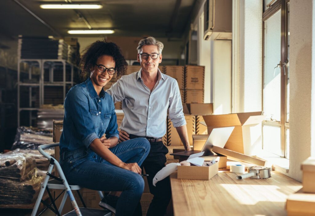 Successful online shop business partners in a small office. Male and female entrepreneurs at their online shop warehouse looking at camera and smiling. PPP and ERC