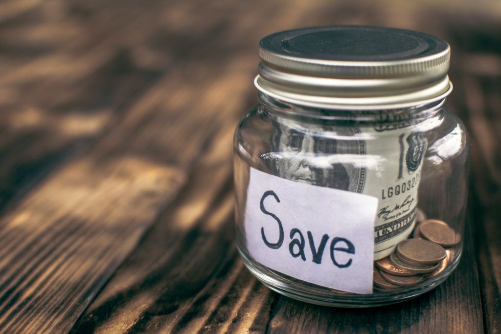 close-up of currency in glass jar with text reading "save" on wooden table. dcap and health fsas